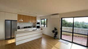 A modern kitchen with a central island, wooden cabinets, pendant lights, and a large sliding glass door to a deck.
