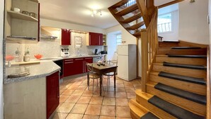 Une cuisine avec des meubles de rangement rouges, un escalier en bois et un sol carrelé.