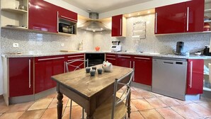 Une cuisine moderne avec des meubles de rangement rouges, un four à micro-ondes, une cuisinière, une machine à café et un lave-vaisselle.