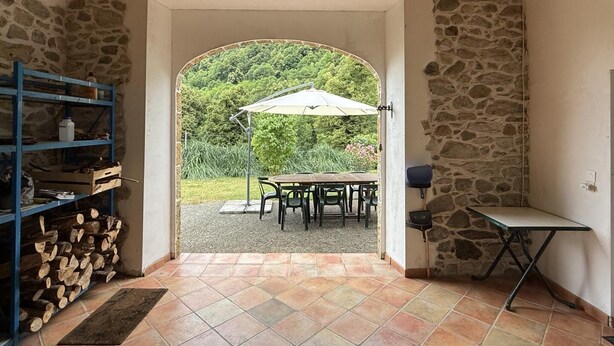 Une porte ouverte donne sur un patio extérieur agrémenté d’une table et de chaises, le tout étant entouré de murs en pierre et surmonté d’un plafond en bois.