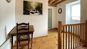 Un intérieur en bois avec une table et des chaises, un tableau représentant un ruisseau de forêt, un plafond en bois et une vue à travers une porte.