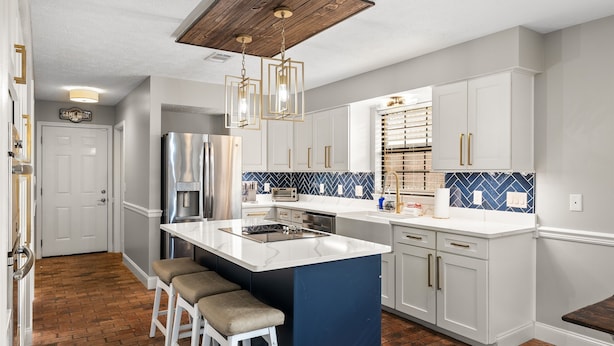 A modern kitchen with white cabinetry, a central island with stools, a built-in oven, and a blue backsplash. - Tropical Feel, Heated Pool, Hot Tub, Game Room, Mini Golf (Panama city beach)