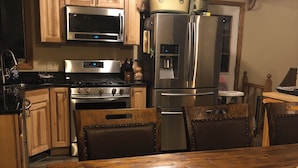 A kitchen with wooden cabinets, stainless steel appliances, a wooden dining table, and a refrigerator with a water dispenser. - Clearfield Co Rockton PA - Cabin Escape (Rockton)
