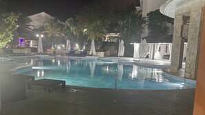 A nighttime pool area with lounge chairs and umbrellas, surrounded by palm trees and buildings. - Tranquil resort with 2 bedrooms and AC, WiFi in Puerto Plata (Puerto Plata)