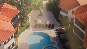 An aerial view of a resort with a large central pool, multiple lounge areas with umbrellas, and surrounding buildings with red-tiled roofs. - Tranquil resort with 2 bedrooms and AC, WiFi in Puerto Plata (Puerto Plata)