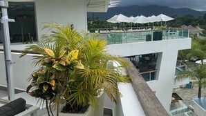 A modern hotel balcony with a view of the mountains, a glass railing, and outdoor seating with umbrellas. - Tranquil resort with 2 bedrooms and AC, WiFi in Puerto Plata (Puerto Plata)