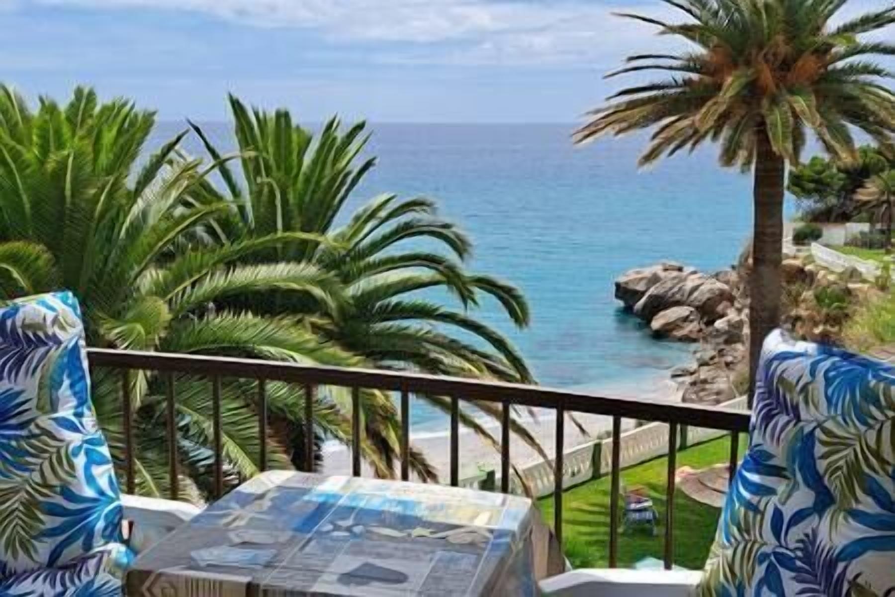 A balcony with a view of the sea, palm trees, and a rocky shoreline.