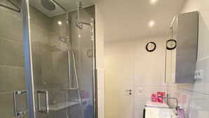 Een moderne badkamer met een douchecabine van glas, een witte wastafel met spiegel erboven en een toilet.