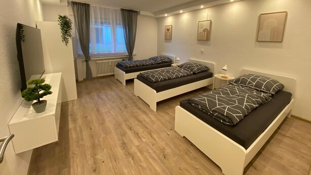 Een moderne slaapkamer met twee eenpersoonsbedden, een klein bureau, een radiator en een raam met gordijnen.