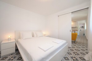 A bedroom with a large bed, white nightstands, and a bathroom visible through an open door. - Beachfront apartments Nincevic (Trogir)
