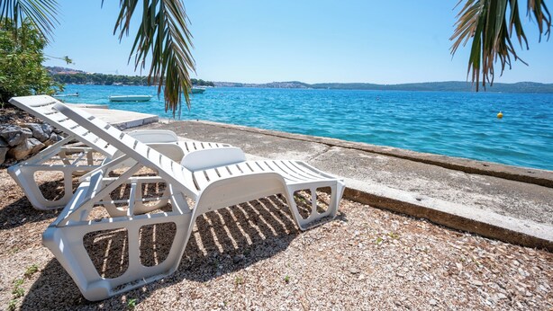 A beachside area with white lounge chairs and a pebble beach. - Beachfront apartments Nincevic (Trogir)