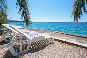 A beachside area with white lounge chairs and a pebble beach. - Beachfront apartments Nincevic (Trogir)