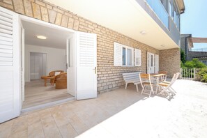An open patio with a wicker chair and a wooden table, a stone wall, and a white door leading inside. - Beachfront apartments Nincevic (Trogir)