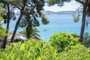 A coastal view with a boat on the water, surrounded by trees and greenery. - Beachfront apartments Nincevic (Trogir)