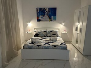 A modern bedroom with a geometric patterned bedspread, a white headboard, and a painting above the bed. - Vacation home in the heart of Naples newly renovated 2 bedrooms and 2 bathrooms (Napoli)