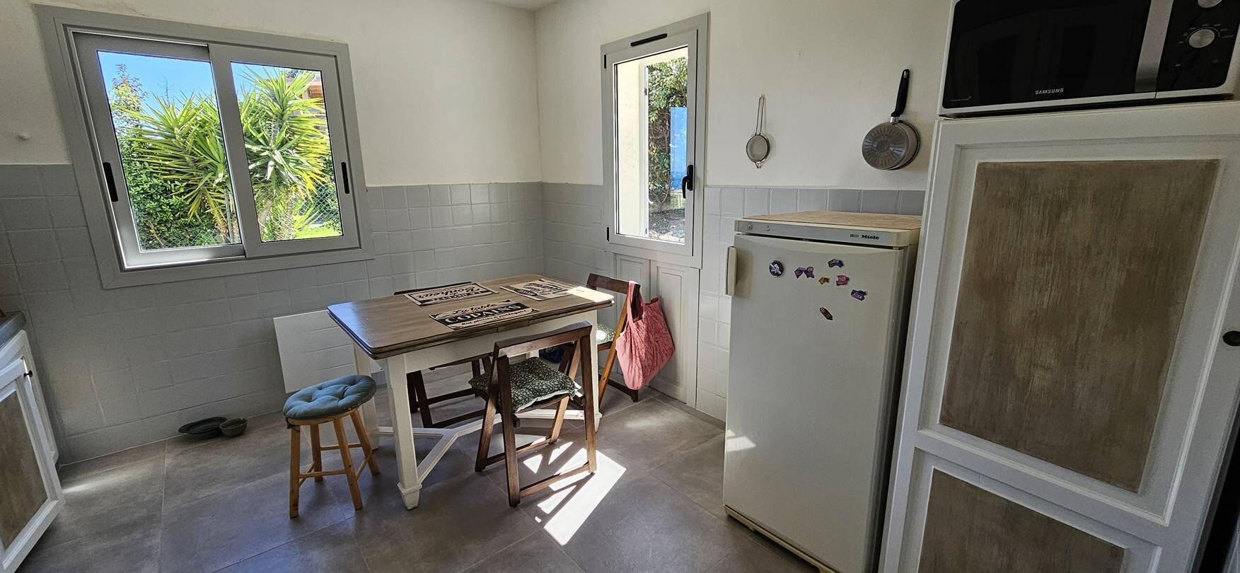 A compact kitchen with a window, a refrigerator, and a dining table with stools.