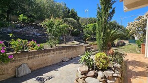 A garden with a stone wall, various plants, and a paved area. - BELLA VISTA-WIFI-PANORAMIC SEA VIEW (SARI SOLENZARA)