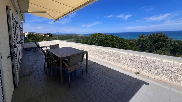 A patio with a table and chairs, a beige awning, and a view of the sea and greenery. - BELLA VISTA-WIFI-PANORAMIC SEA VIEW (SARI SOLENZARA)