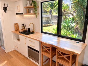 Una cocina moderna con un lavamanos negro, encimera de madera y horno empotrado. Se observa una ventana con vistas a un jardín.