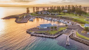 An aerial view of a coastal marina with boats, a lighthouse, and a building with a blue roof.