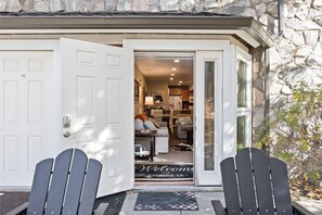 L'ingresso di una casa con un tappetino, due poltrone Adirondack e vista su un soggiorno con un divano e un tavolino.