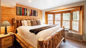 Ein Bett mit Holzrahmen, einer weißen Matratze und einem Holz-Kopfende, sowie ein Fenster mit Blick ins Freie.