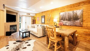 Ein gemütliches Wohnzimmer mit Kamin, Holzwänden, einem Esstisch und einer Couch.
