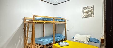 Quarto de dormitório com beliches, ventilador de teto e uma estátua de Buda na parede.