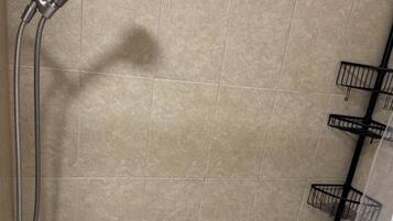 A bathroom with beige tiles, a white bathtub, a shower with a handheld showerhead, and black towel racks.