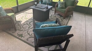 Un patio con mobiliario de mimbre, un tapete estampado y vista a un jardín.