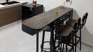 Cuina compacta amb taula i cadires de fusta, un rentapeus i un petit aparell negre.
