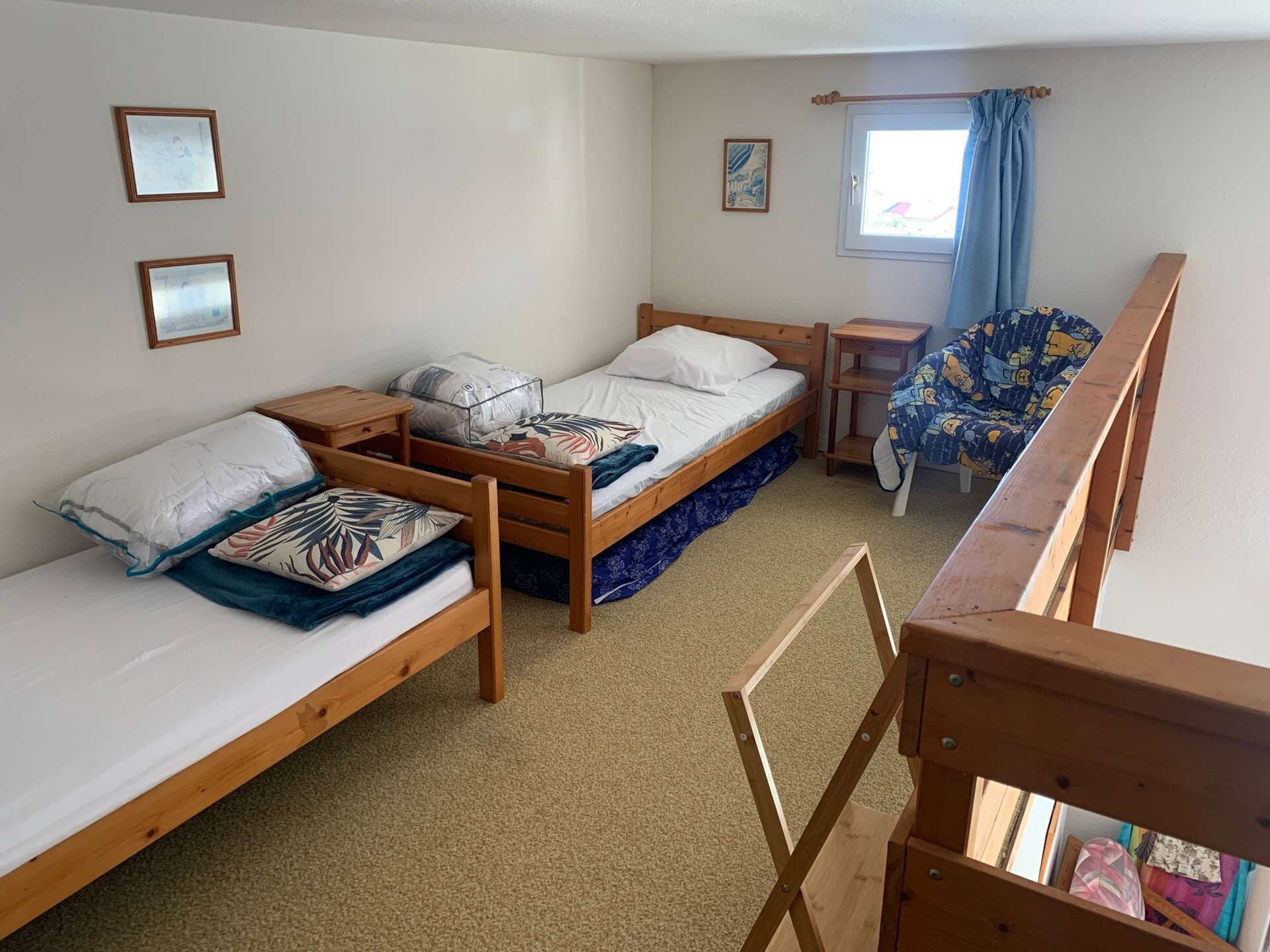Une chambre de type dortoir avec deux lits simples, une petite table, une chaise et une fenêtre avec des rideaux.