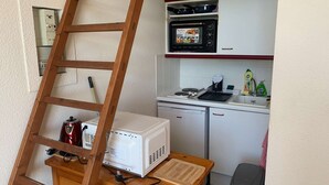 Eine Küche mit Mikrowelle, kleinem Kühlschrank und einem Holztisch mit einem weißen Gerät darauf.