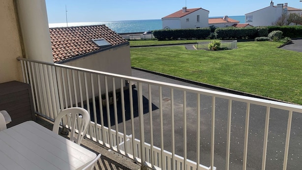 Ein Balkon mit weißer Brüstung, Tisch und Stühlen. Im Hintergrund ist ein gepflegter Rasen und ein Gebäude mit rotem Ziegeldach zu sehen.