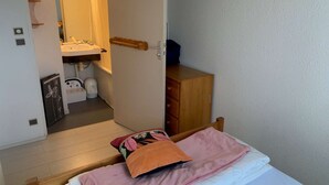 Ein Schlafzimmer mit Bett, einem Holzschrank, einem Badezimmer mit Waschbecken und Spiegel sowie einer Tür zu einem anderen Raum.
