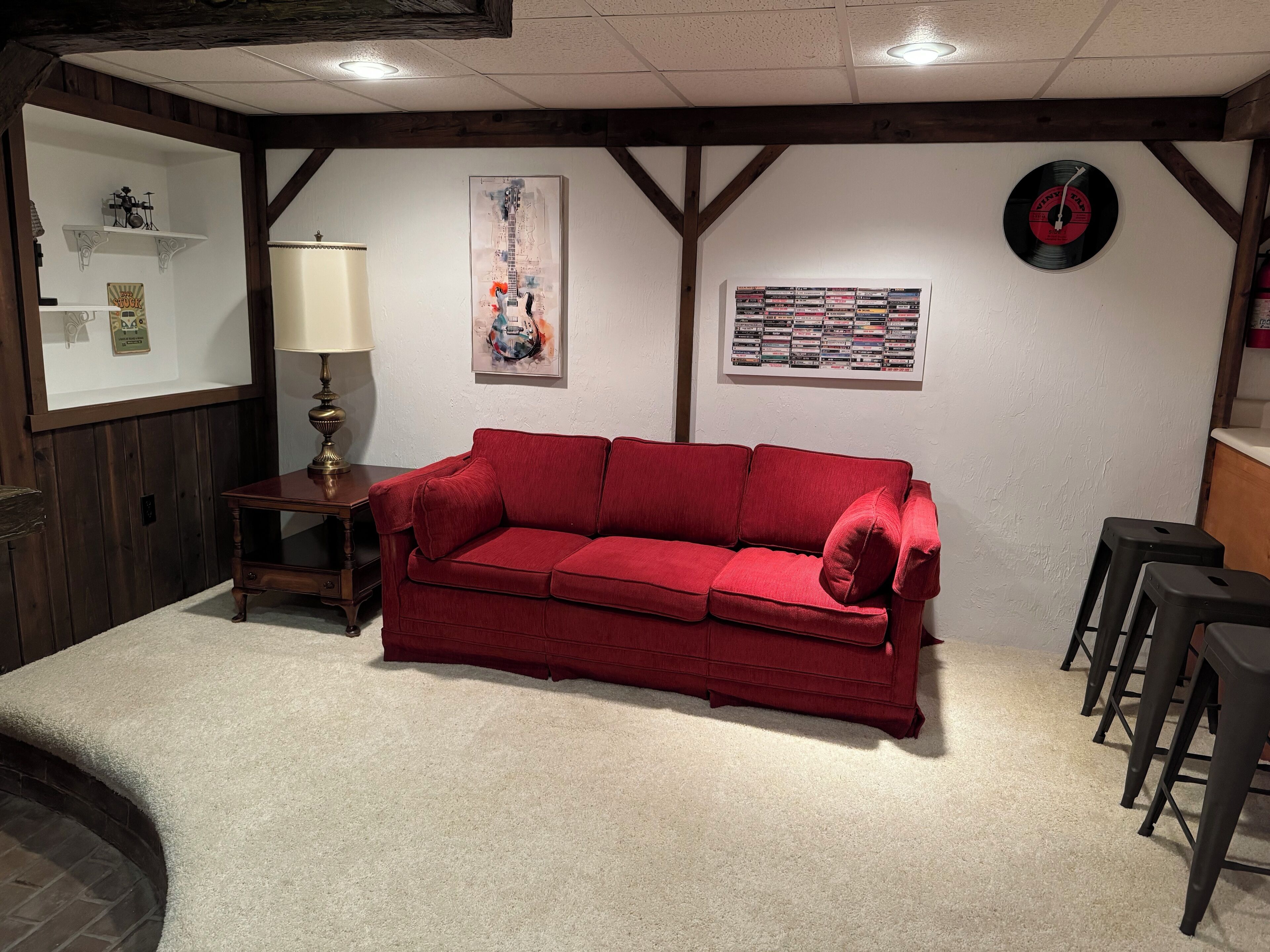 A cozy living room with a red sofa, a lamp, a wall-mounted record player, and a collection of vinyl records.