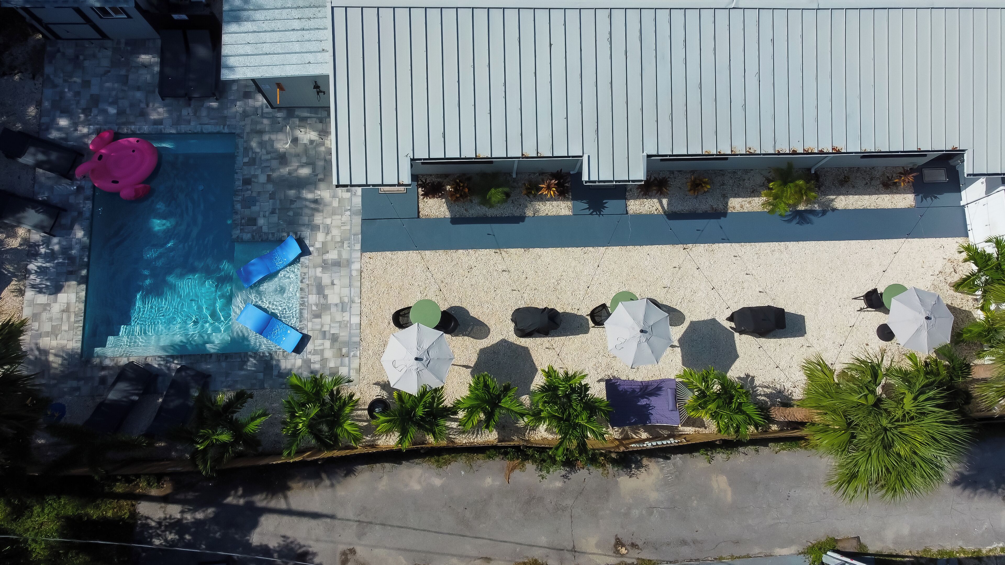 An aerial view of a pool area with lounge chairs, umbrellas, and a pink flamingo float.