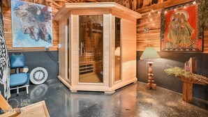 Un sauna avec des murs en bois et une porte en verre, une chaise bleue, une horloge et une lampe décorative.