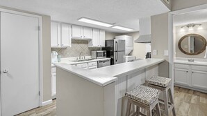 Una cocina moderna con armarios blancos, una isla central y taburetes de bar.