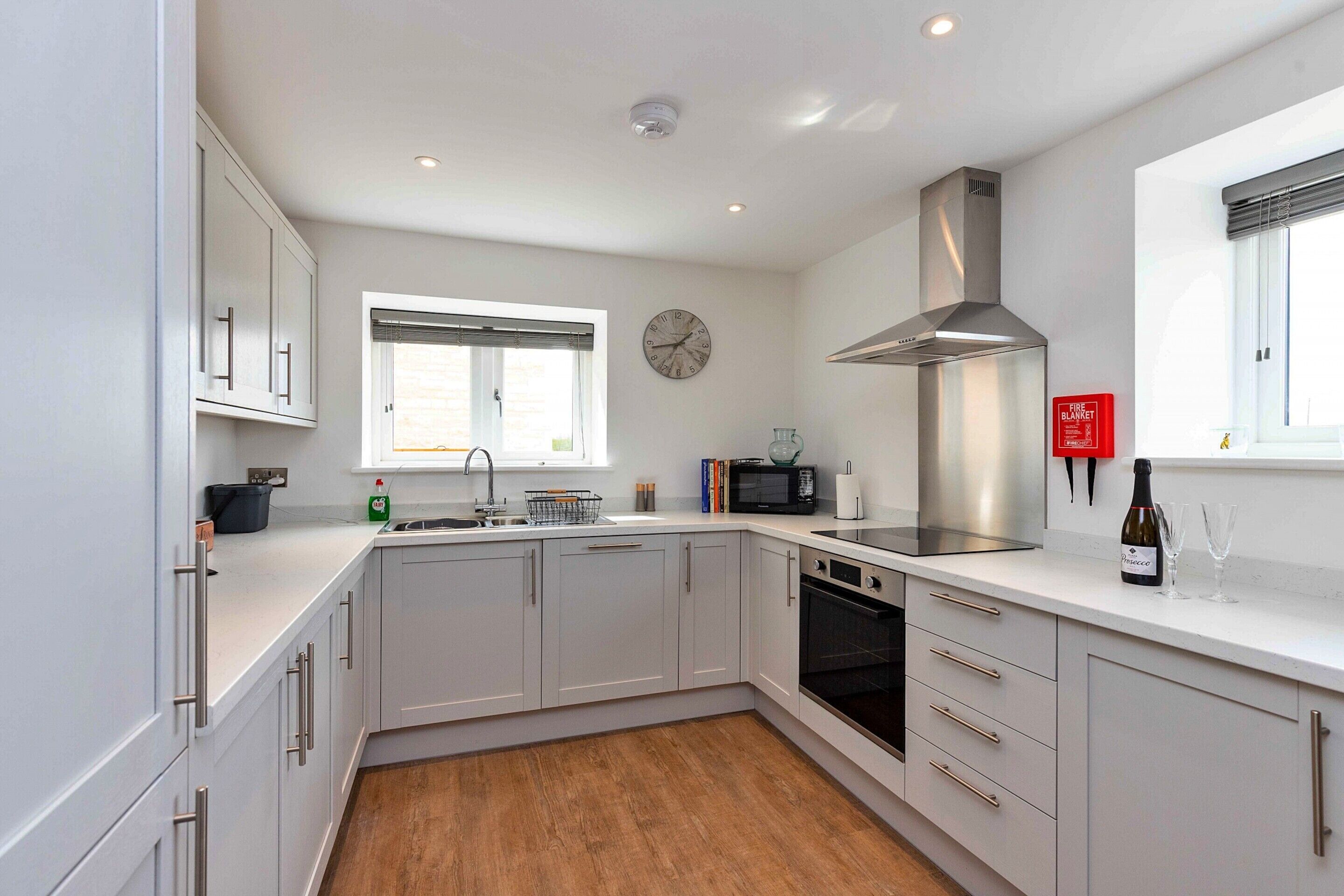 A modern kitchen with white cabinets, a stainless steel range hood, a microwave, and a clock on the wall.