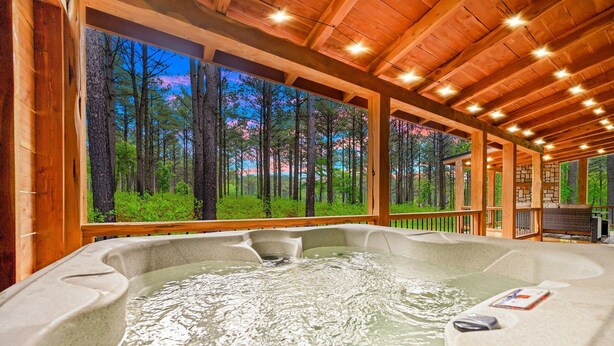 A hot tub with a view of a forest through large windows.