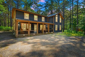 A two-story cabin with a porch, surrounded by a forest.