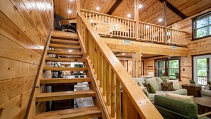 A wooden interior with a central staircase, a sofa, and a dining area.