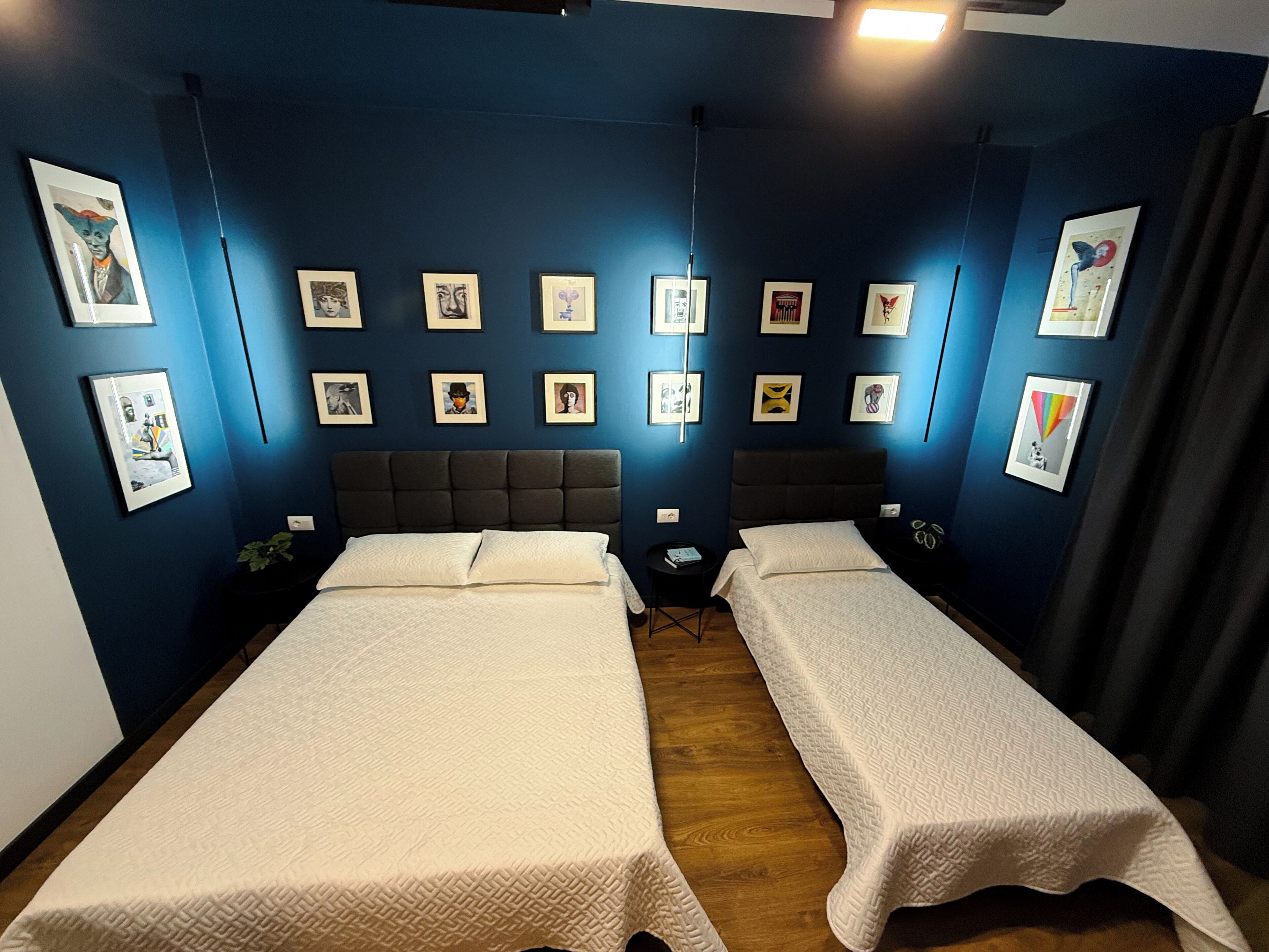 Een kamer met twee bedden, een donkerblauwe wand en meerdere ingelijste foto’s.