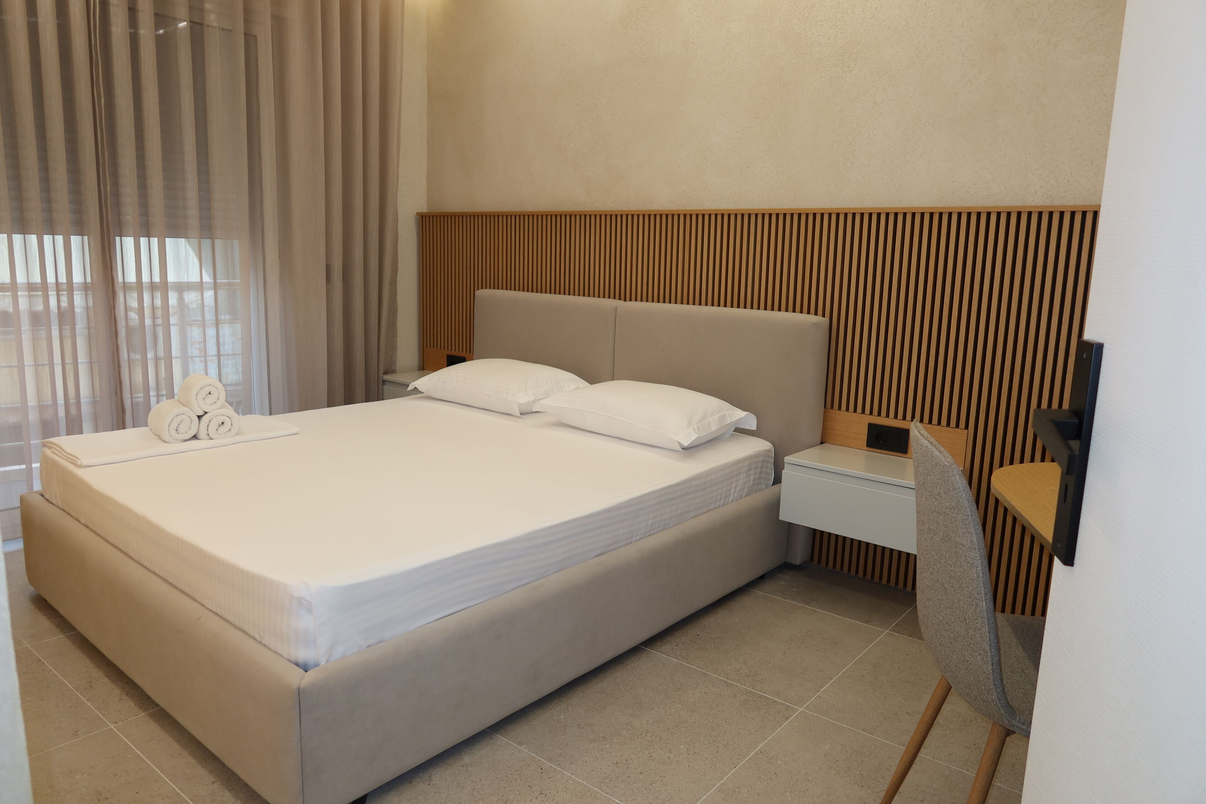 A hotel room with a large bed, a bedside table, a chair, and a wooden panel wall.