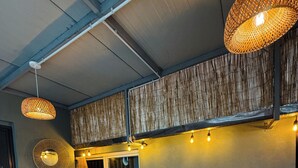 Una habitación acogedora con un sofá y dos palets de madera que sirven como asiento, una lámpara colgante tejida y una ventana con cortinas.