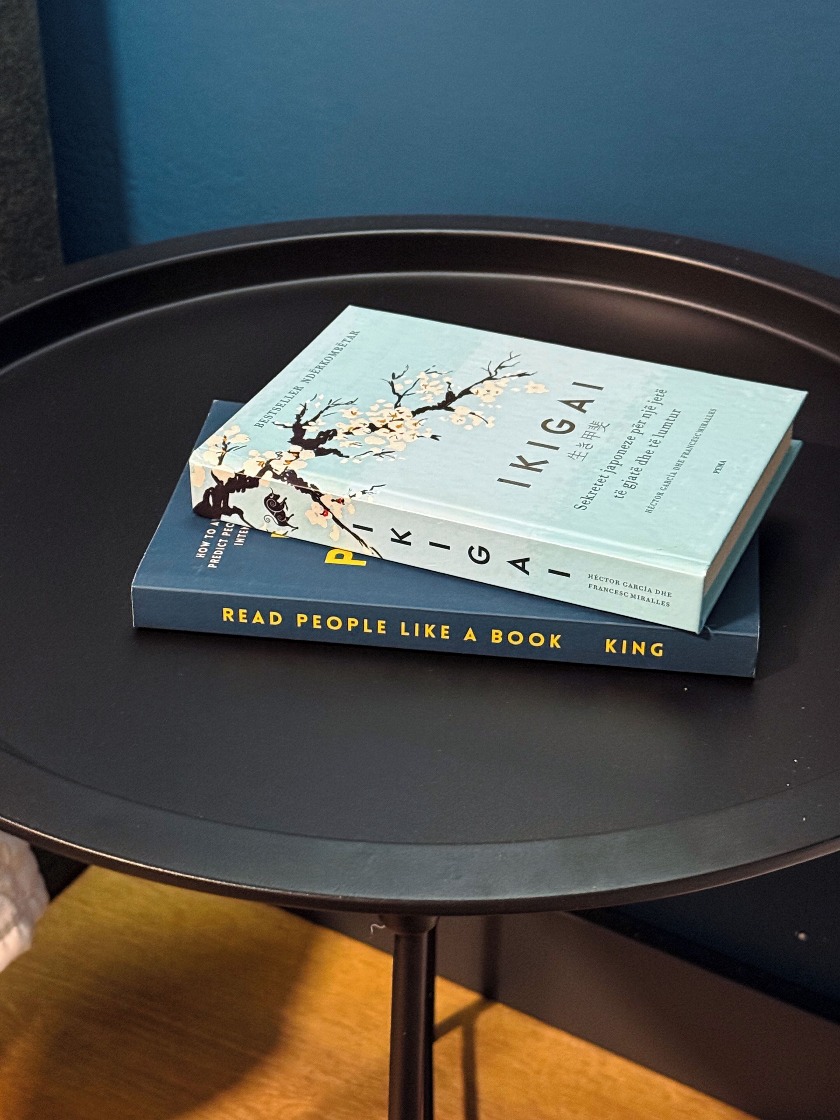 Zwei Bücher mit den Titeln 'Ikigai' und 'Menschen wie offene Bücher' auf einem schwarzen runden Tisch.
