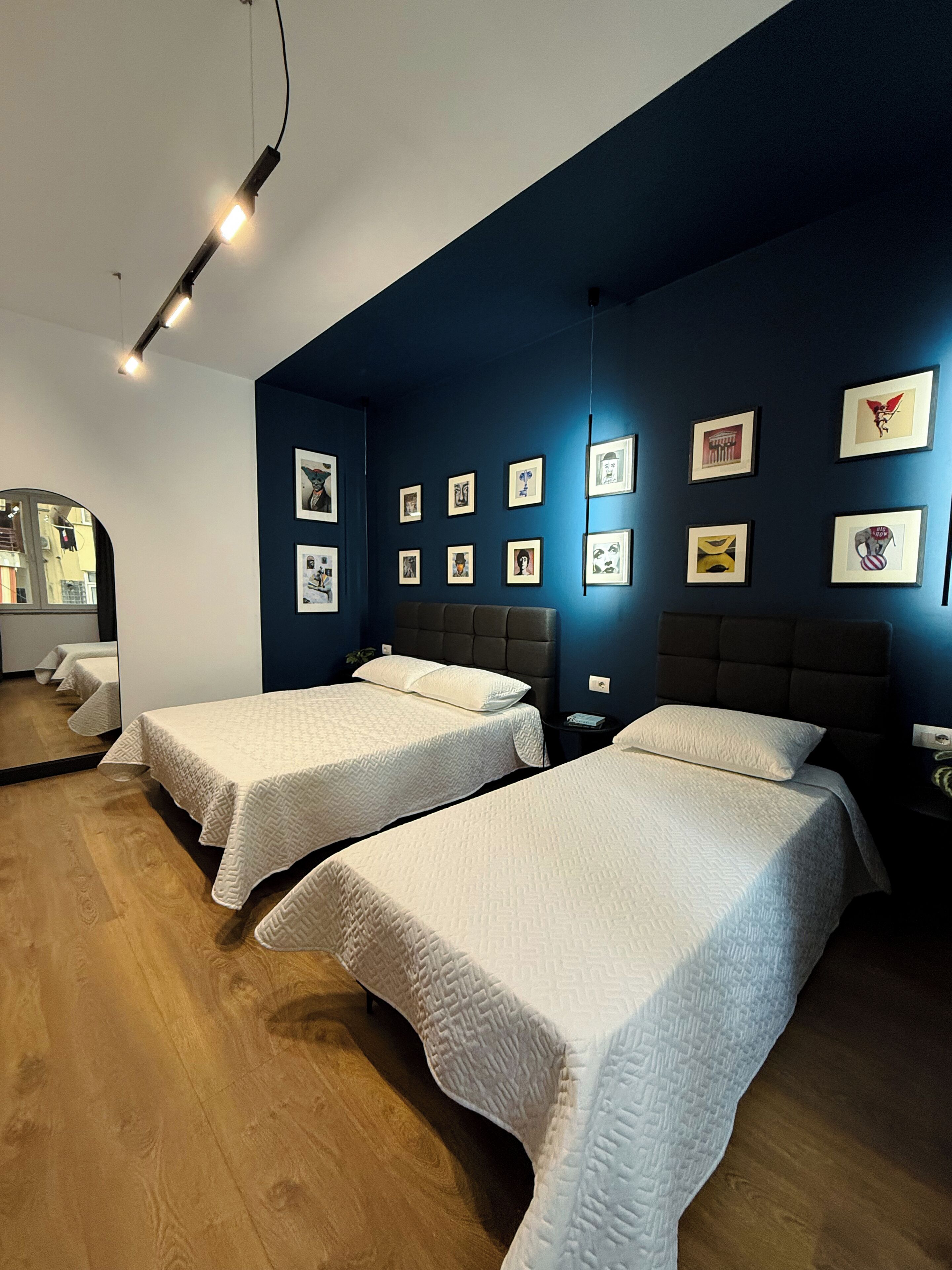 Una habitación de hotel con dos camas, una pared de acento azul oscuro y varias fotografías enmarcadas.