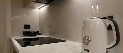 A modern kitchen with a white marble countertop, a black induction cooktop, and a white electric kettle.
