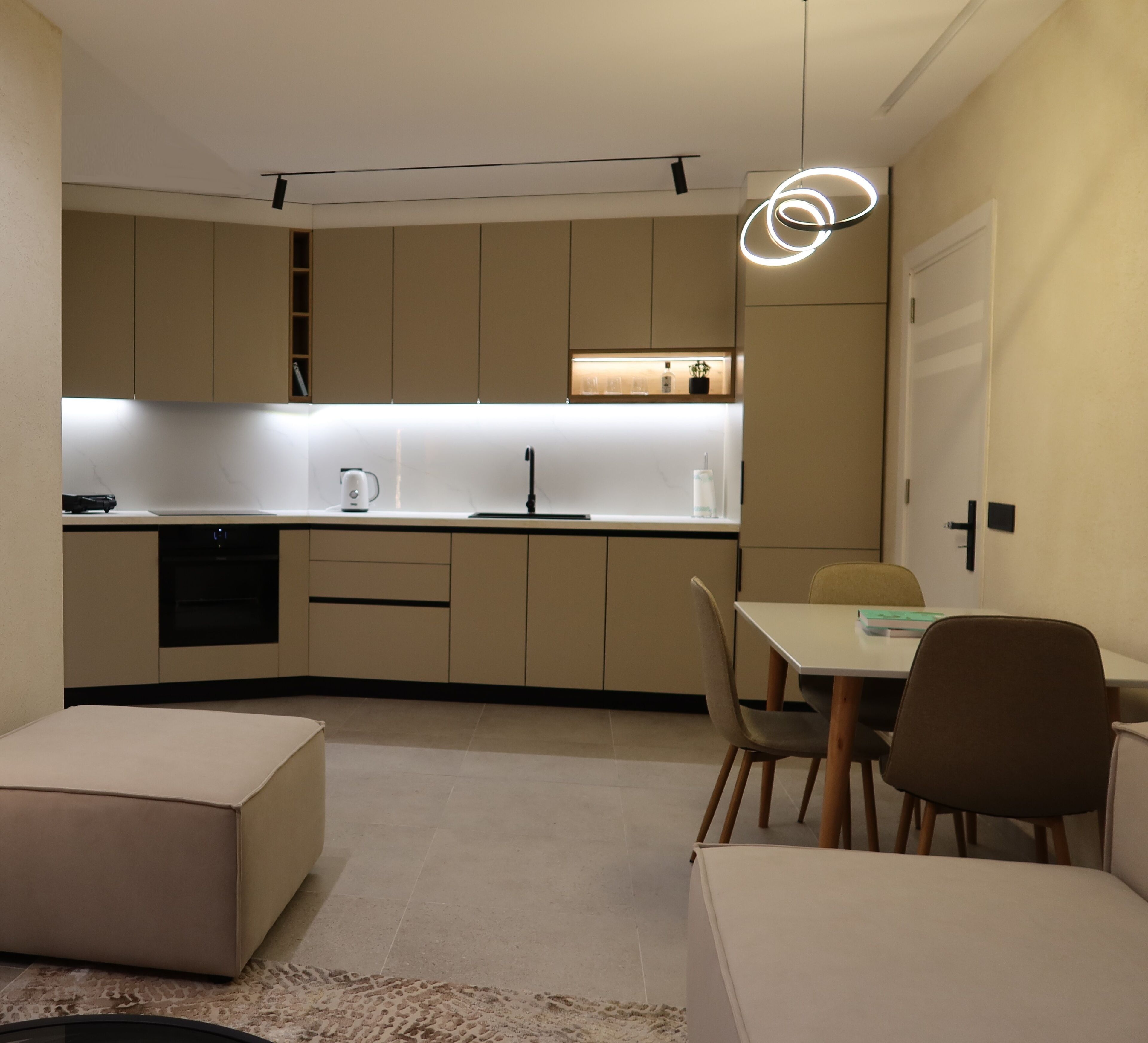 Una cocina moderna con electrodomésticos integrados, un comedor con mesa y sillas, y una zona de estar acogedora con otomanas.